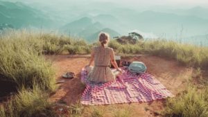Eine Frau sitzt auf einem Berggipfel beim Picknick und relaxed Natur kann uns heilen und entspannen