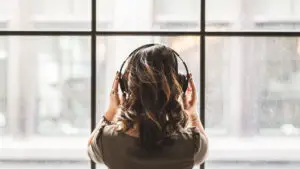 Eine Frau hört Musik via Kopfhörer und blickt dabei aus em Fenster