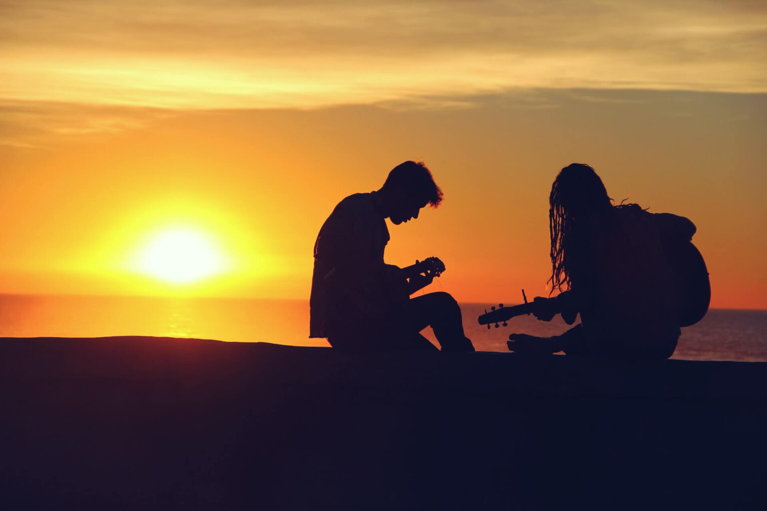 Zwei Menschen spielen bei Sonnenuntergang Gitarre