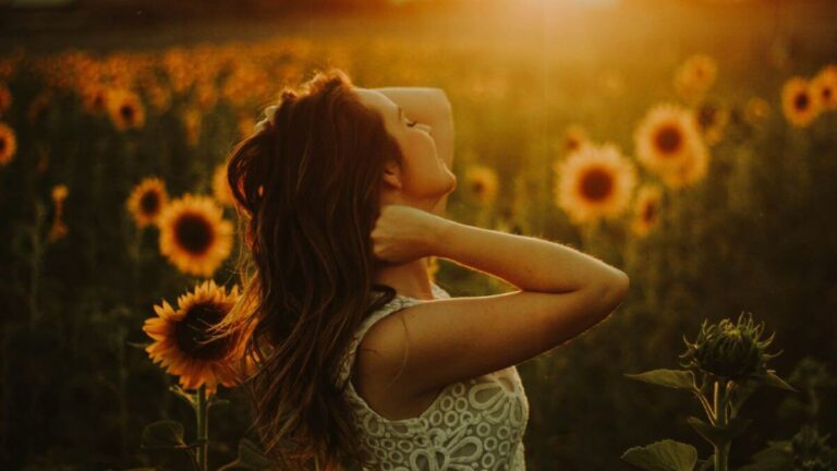 Positive Emotionen in der Natur erleben - eine Frau tanzt durch ein Sonnenblumenfeld